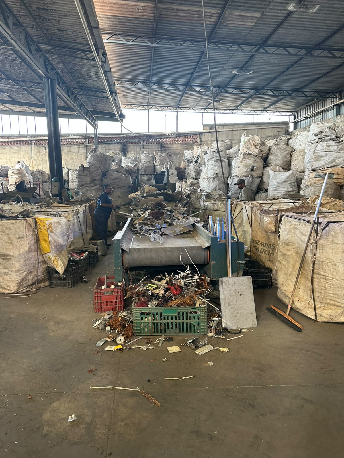 Equipe da E3 trabalhando junto à esteira, com sucata metálica e bags no galpão